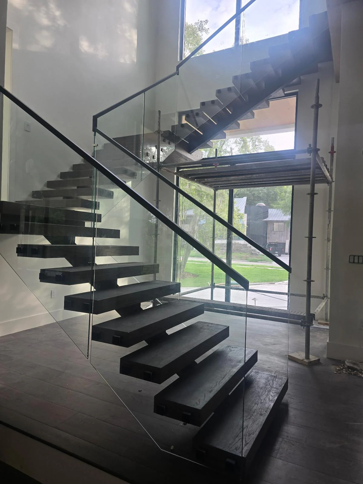 Floating staircase with dark treads, a black metal frame, and glass railings