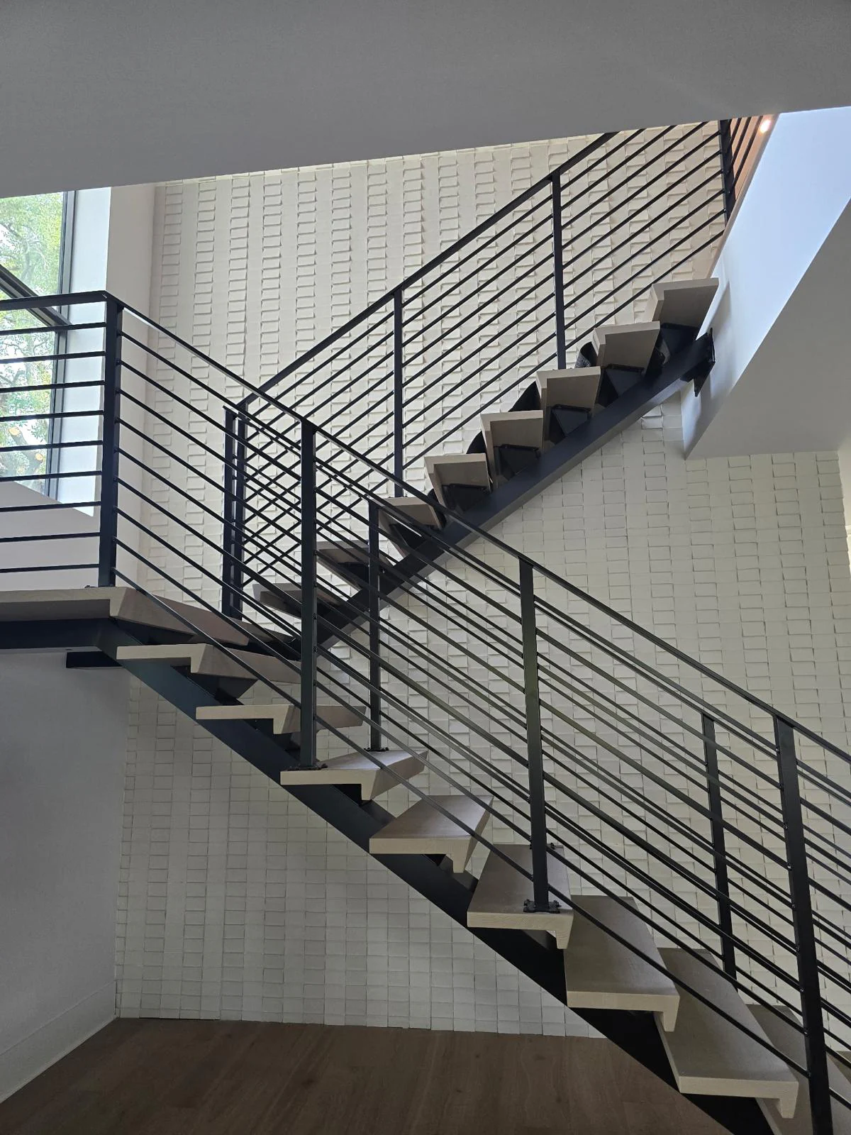 Modern metal staircase with black horizontal railing and light wood treads